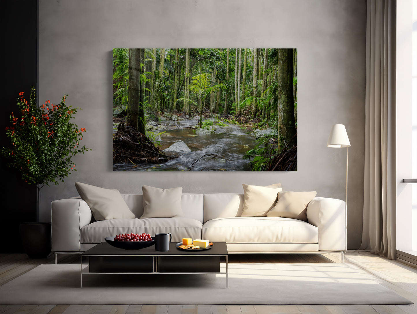 A modern living room with a white sofa, black coffee table, and floor lamp. On the wall hangs the Island of One - Curtis Falls Queensland Rainforest Photography Print. A plant and a bowl of fruit add pops of color to the space.