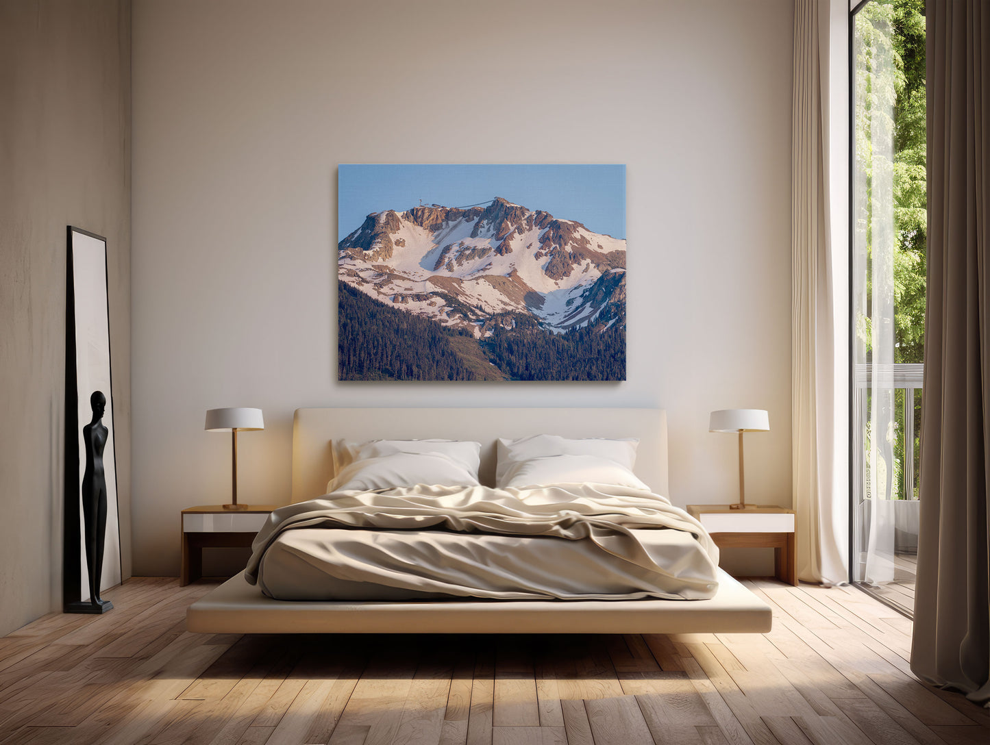A modern bedroom with a low platform bed, beige bedding, bedside tables with lamps, and a floor mirror with a black abstract sculpture. Above the bed hangs Whistler Alpine Glow | Canadian Mountain Wall Art as sunlight filters through tall curtains.