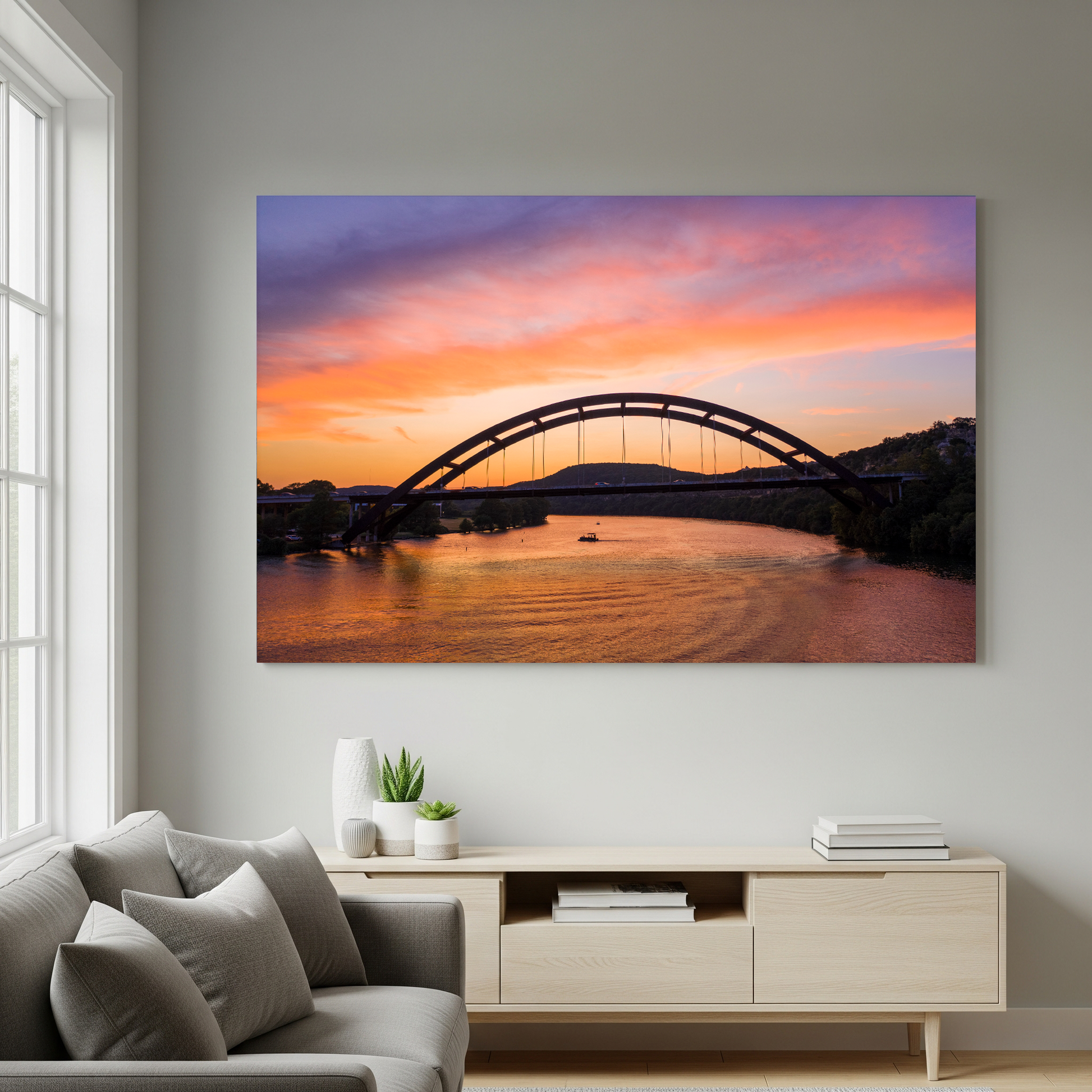 The “Austin Glow | Pennybacker Bridge Wall Art” hangs above a modern white sideboard on a light gray wall in a bright minimalist living room with a gray sofa.