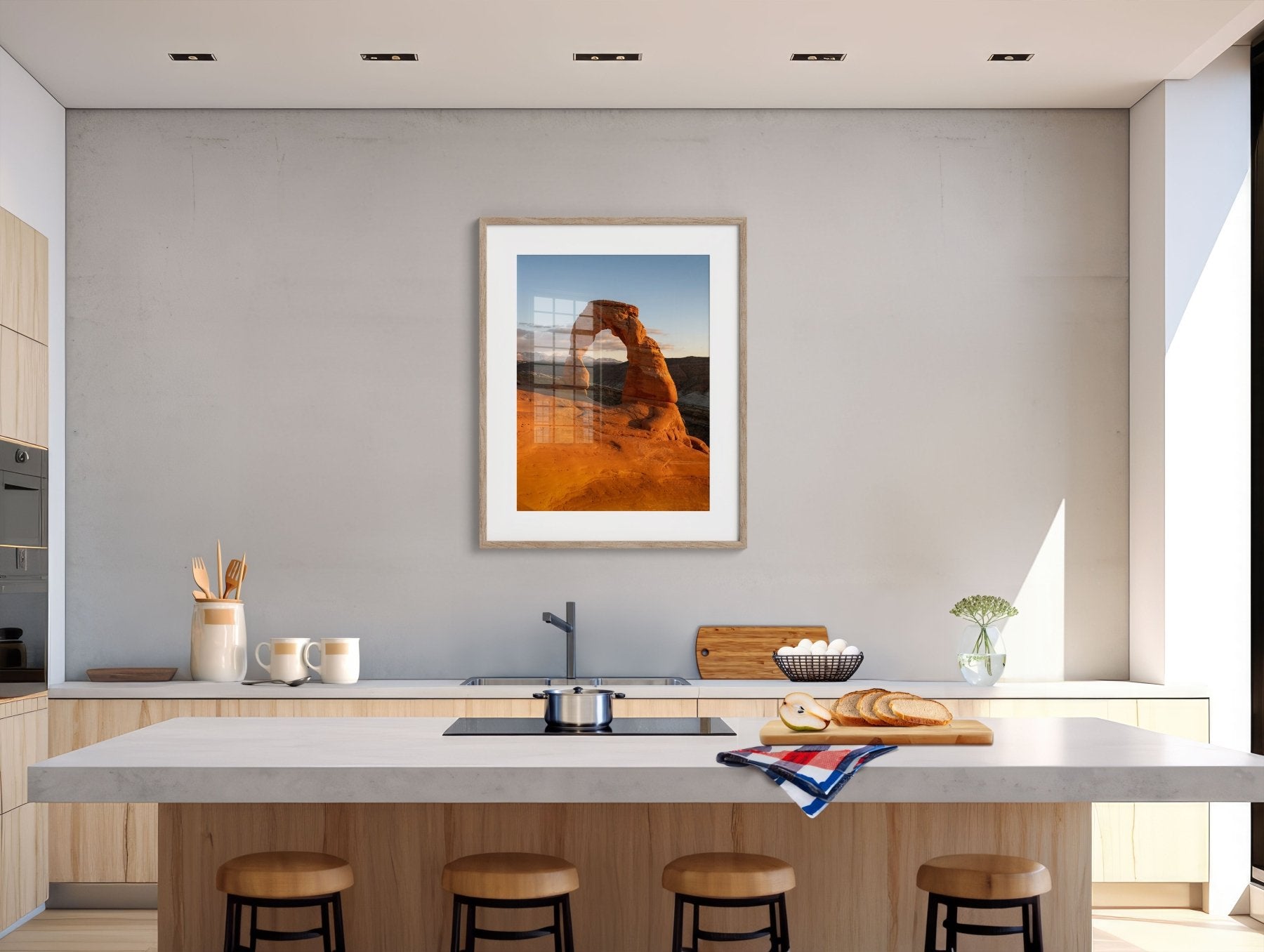 Modern kitchen in light wood and white, featuring a large island with stools, a loaf of bread on a cutting board, and southwest decor highlighted by the Delicate Light | Vertical Delicate Arch Print, Utah above the counter.