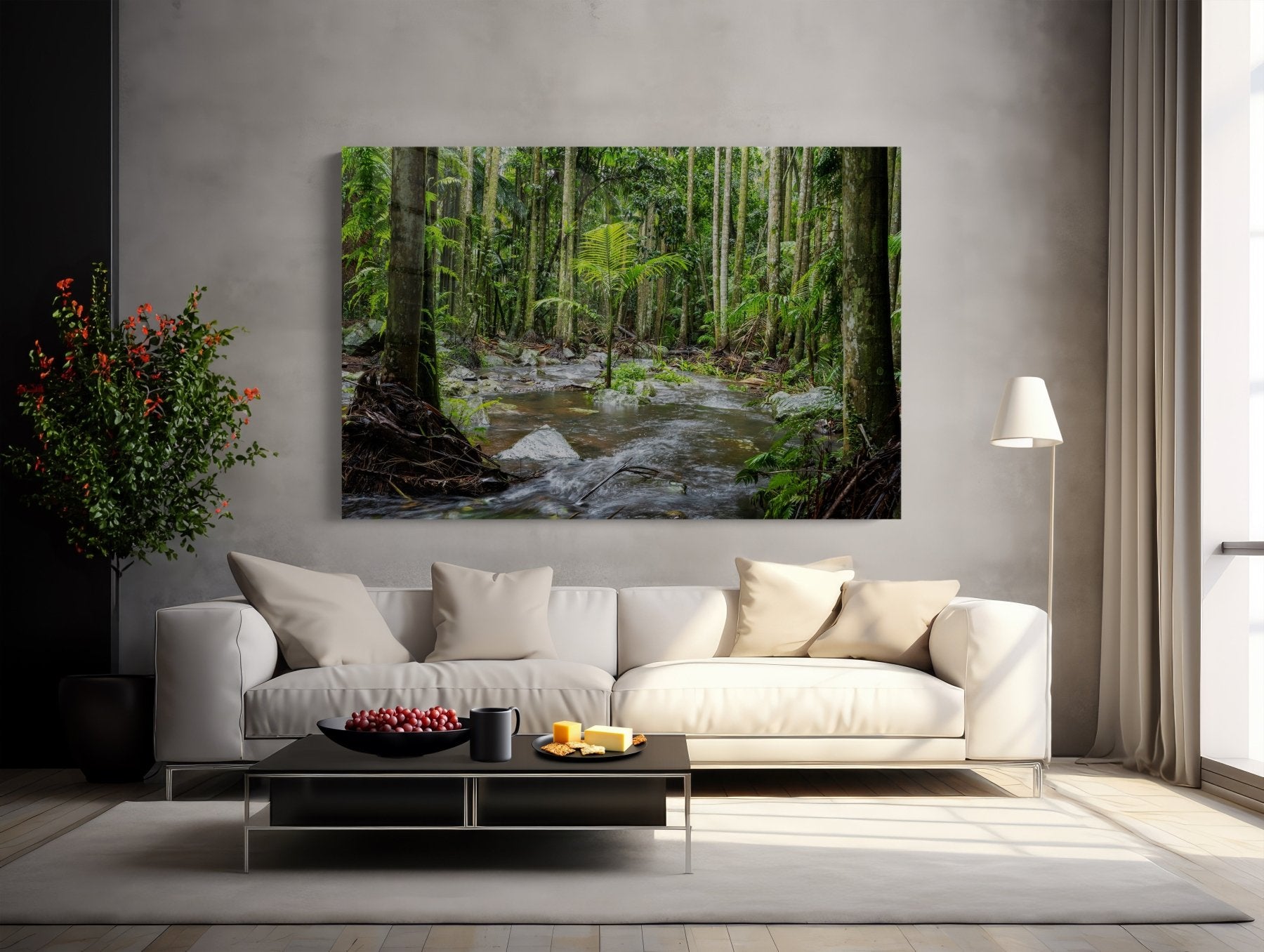 A modern living room with a white sofa, neutral cushions, black coffee table with fruit, potted plant, and floor lamp. Above the sofa hangs the Island of One - Curtis Falls Queensland Rainforest Photography Print.