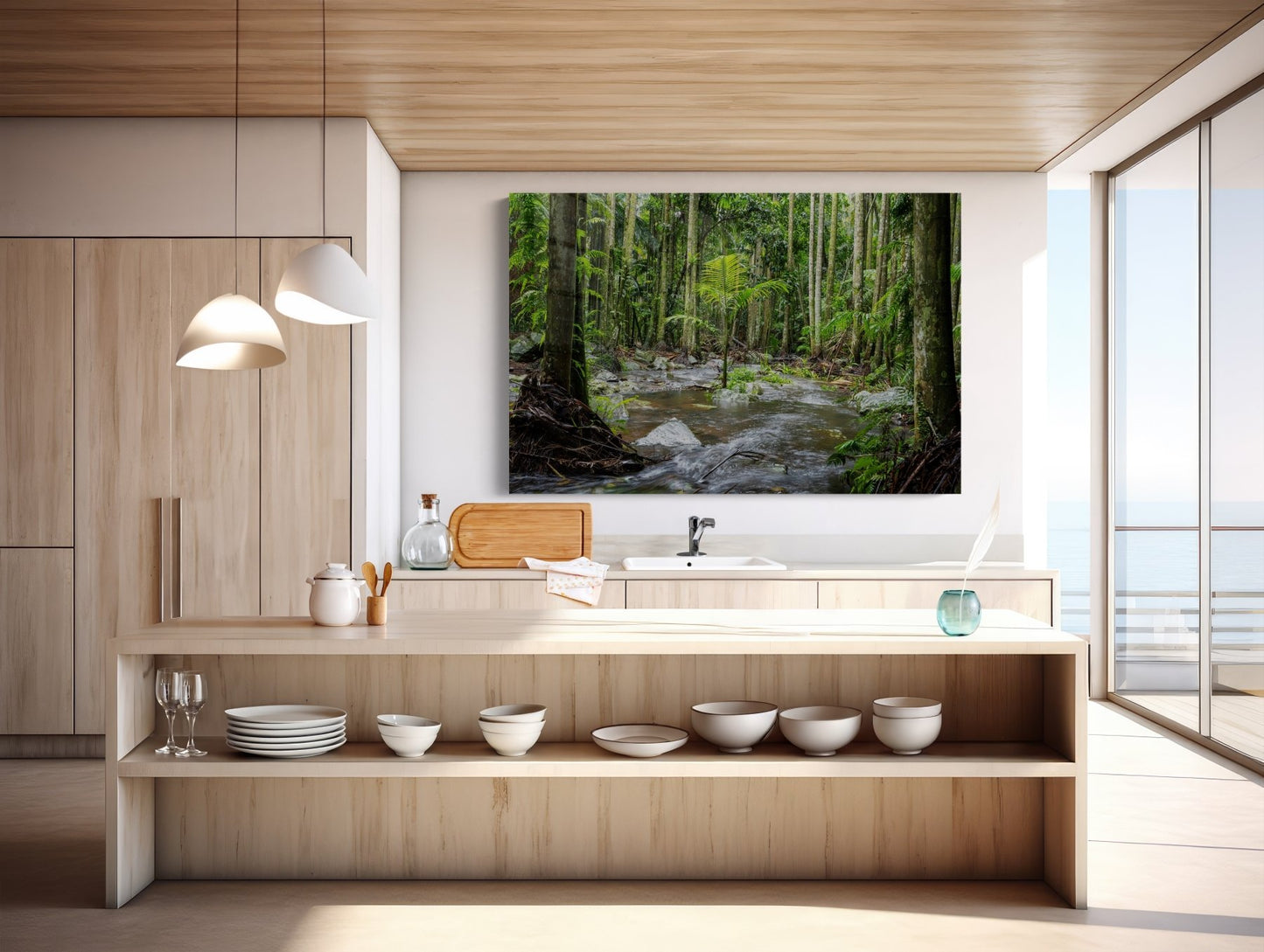 Modern kitchen with light wood cabinets, open shelving, and a large window with ocean views. Above the sink hangs "Island of One - Curtis Falls Queensland Rainforest Photography Print," bringing Australian art to the natural décor. Pendant lights accent the island.