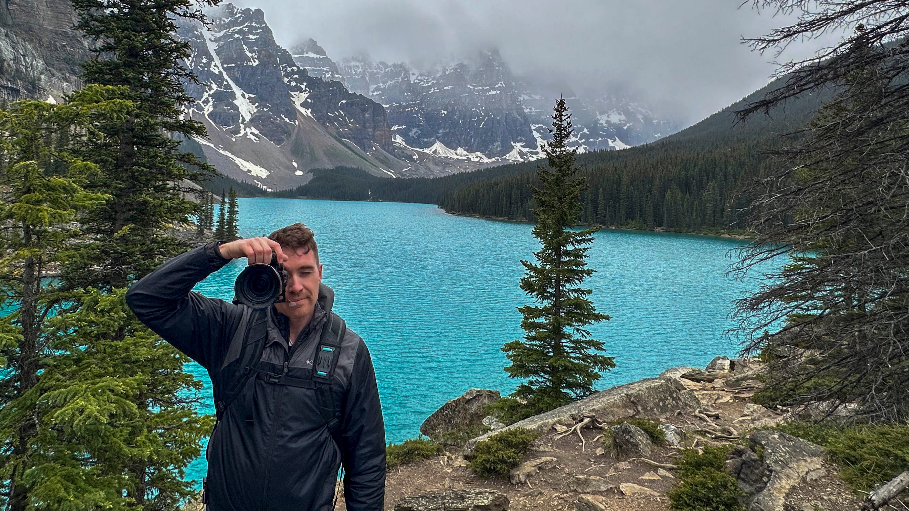 Photographer John Davis taking a photo of a scenic lake with mountains in the background