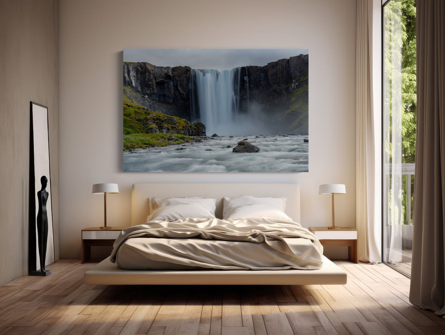 A modern bedroom with a large bed, neutral tones, two bedside lamps, a tall mirror, and a sculpture. Above the bed hangs The Moss Kingdom Falls - Iceland Waterfall Photography Print as sunlight streams through the glass door to greenery.
