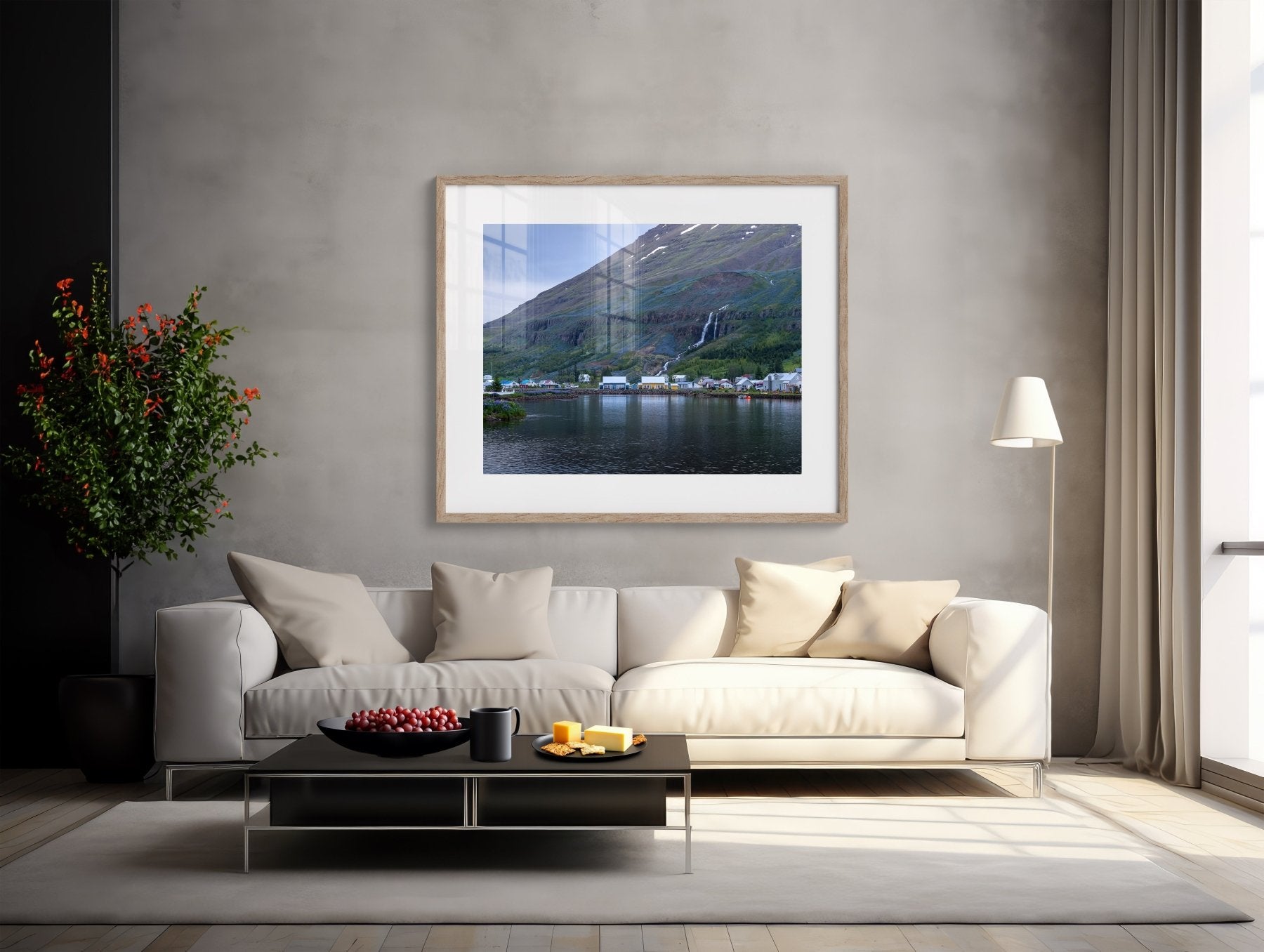 A modern living room with a white sofa, light cushions, black coffee table with fruit, floor lamp, and potted plant. The wall features The Perfect Pair - Iceland Photography Print | Seyðisfjörður Harbor Houses.