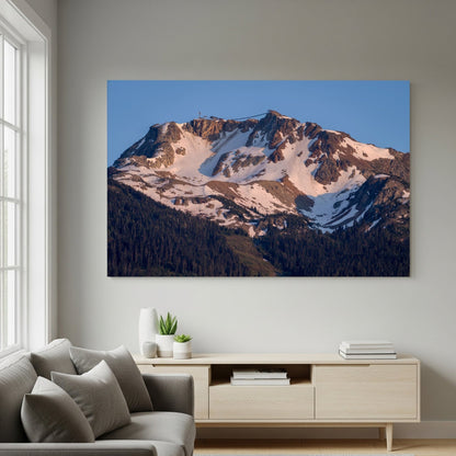 A modern living room features a gray sofa, cushions, and a light wooden console table. Above it hangs "Whistler Alpine Glow | Canadian Mountain Wall Art," capturing Whistler Mountain at sunset. Natural light streams through the window.