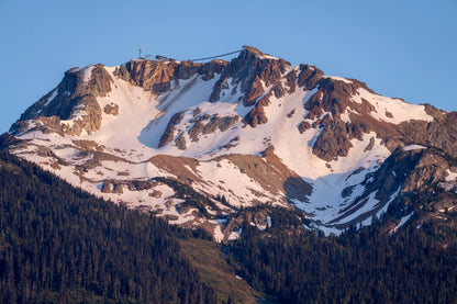 Whistler Alpine Glow | Canadian Mountain Wall Art depicts snow-capped peaks, rocky terrain, a small summit structure, and a cable car above forested slopes beneath a clear blue sky—showcasing Whistler Mountain’s stunning beauty.