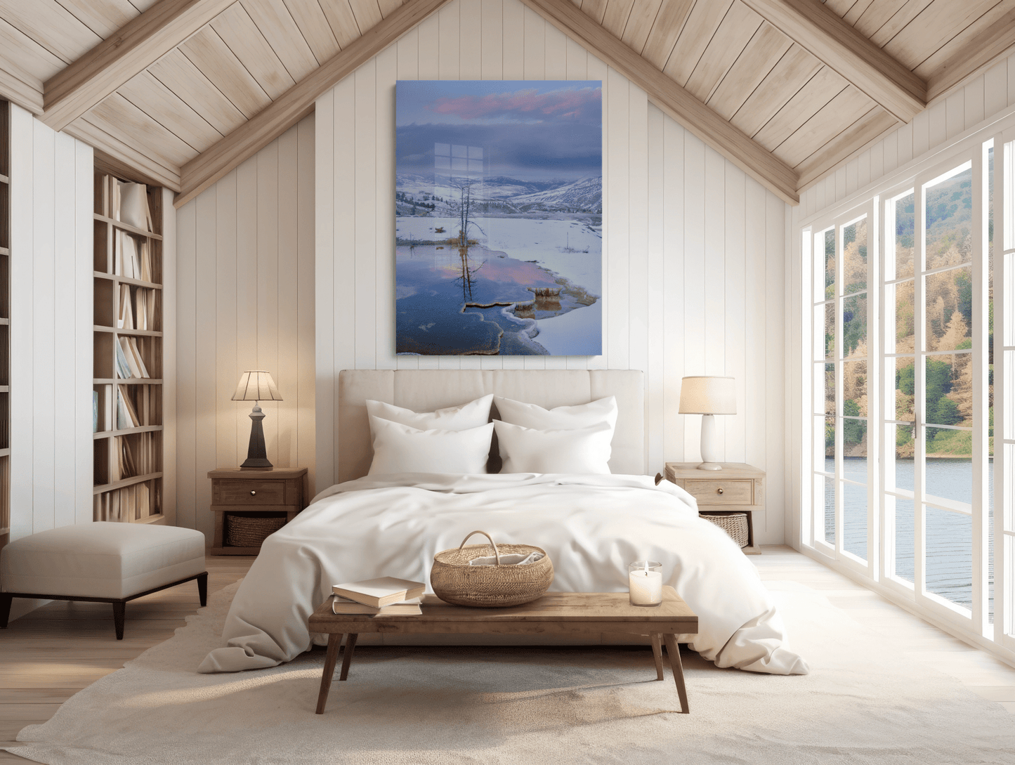 A cozy bedroom with a vaulted wooden ceiling, large bed, bedside tables with lamps, bookshelves, and tall windows with a lakeside view. Above the bed hangs "Winter's Water Color - Mammoth Hot Springs Yellowstone Photography Print.